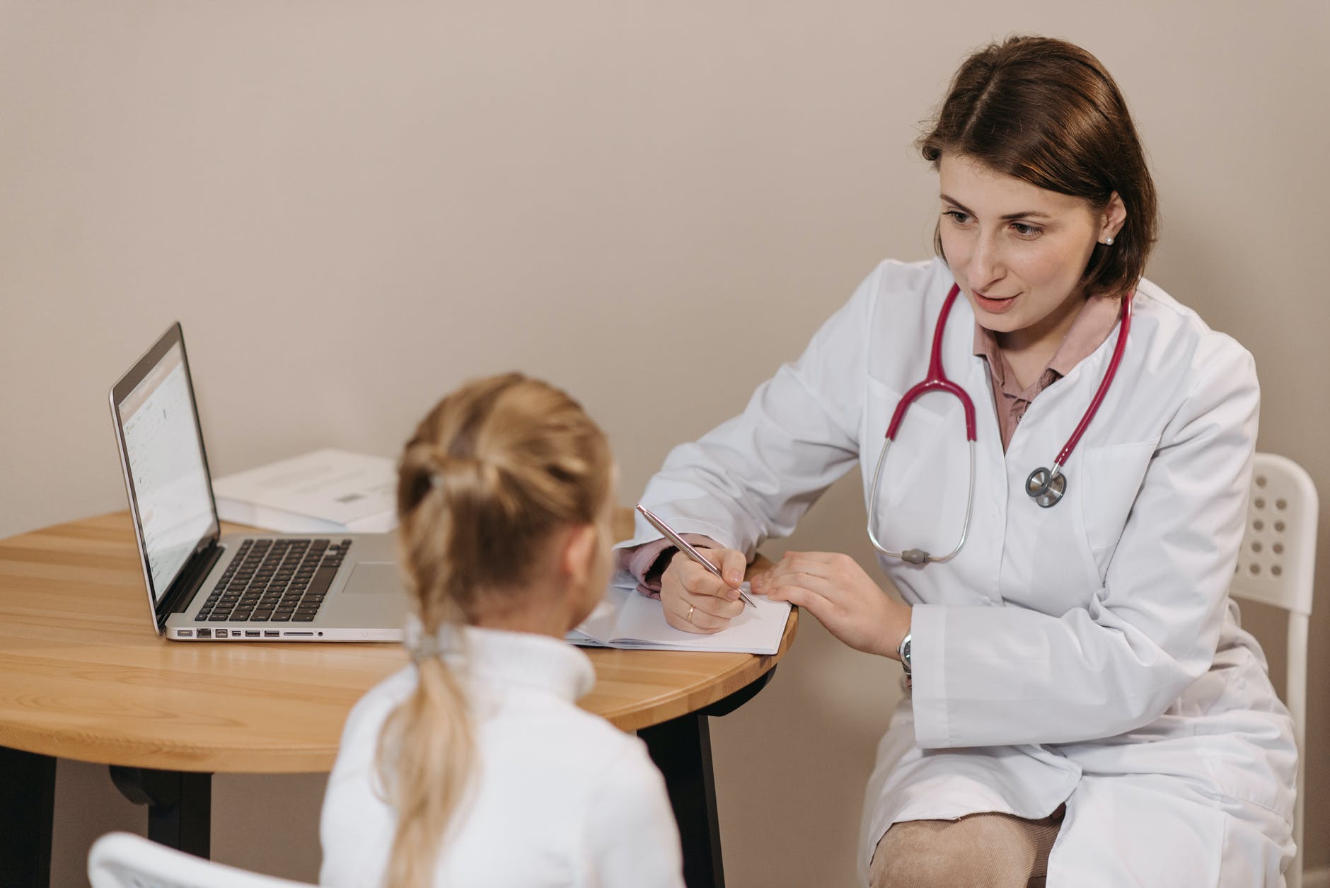 woman in white lab coat listening to a girl and writing down notes